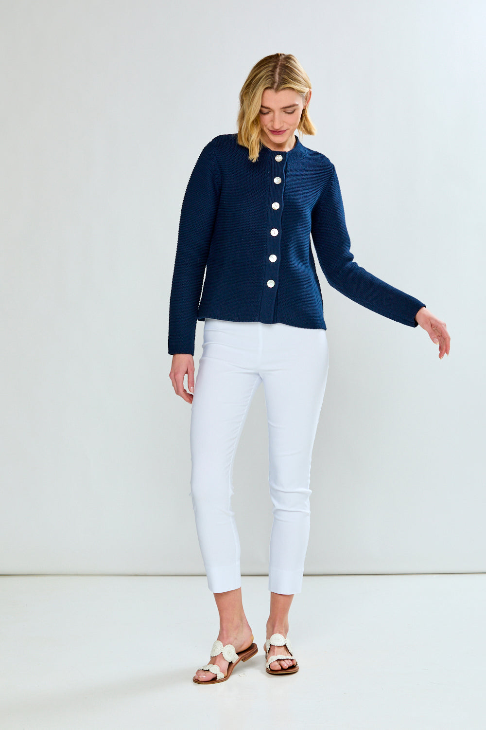 Woman wearing a navy cardigan and white pants on a white background