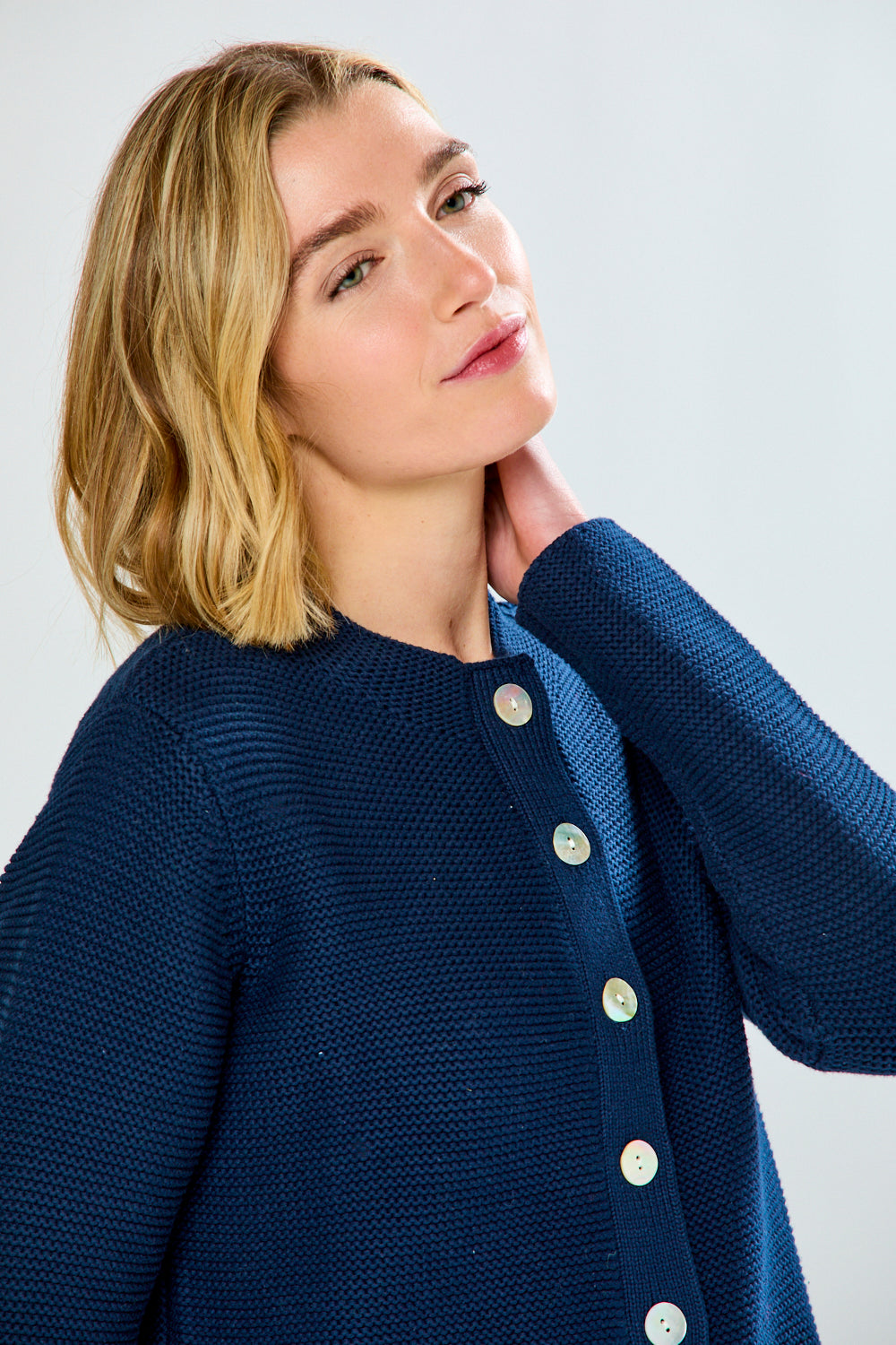 Woman wearing a blue textured cardigan with button details on a white background