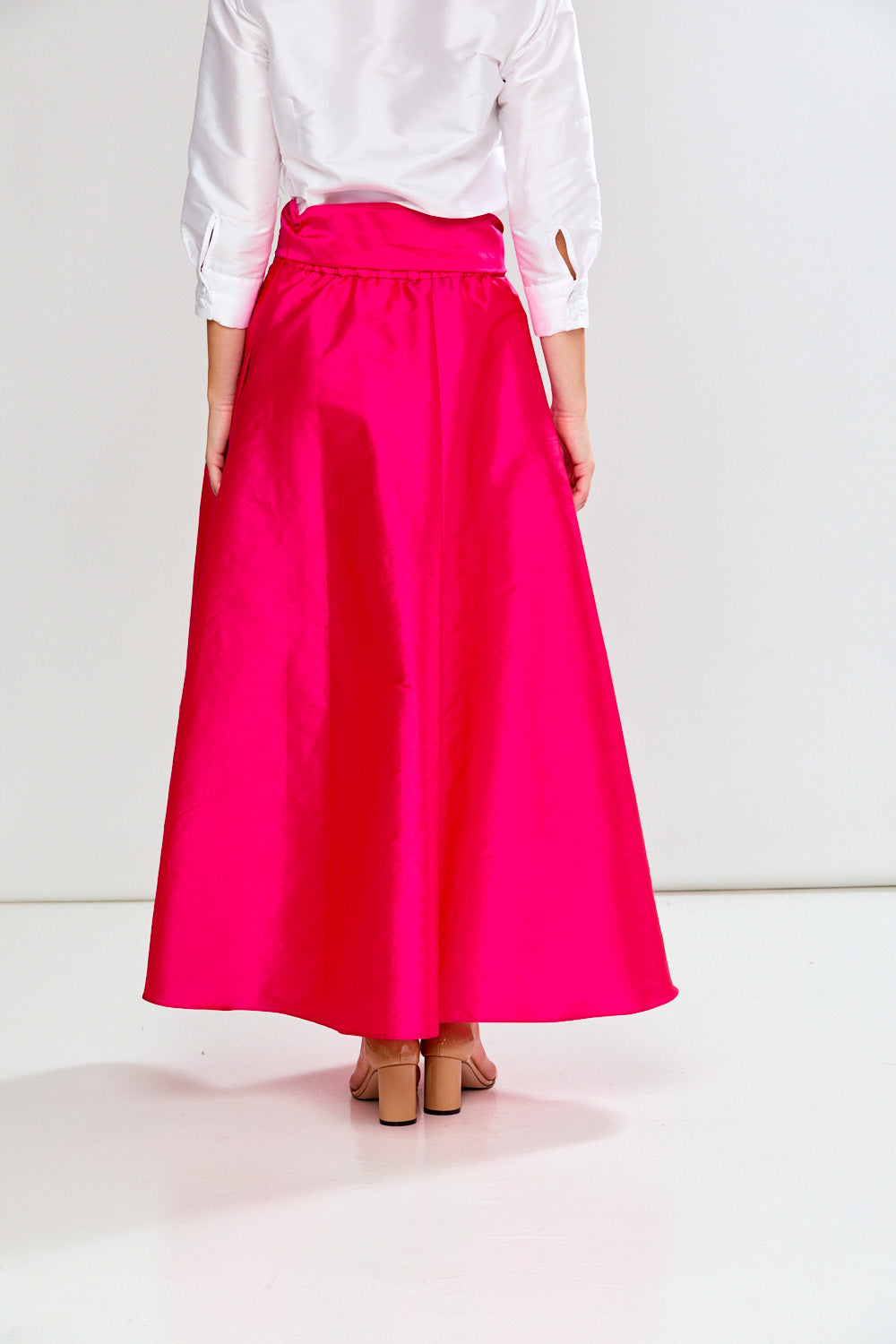 Person wearing a bright pink skirt and white shirt on a light background