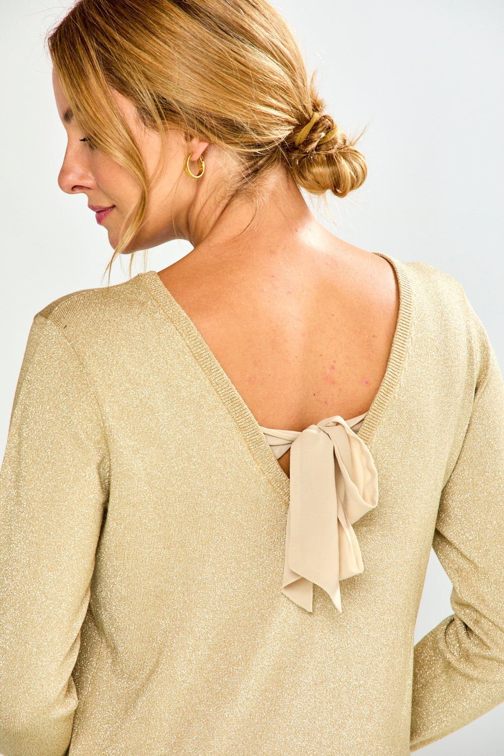 Woman wearing a gold sweater with a bow detail on a plain background