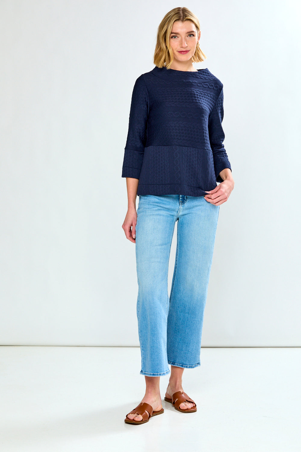 Woman wearing a navy sweater and light blue jeans on a white background