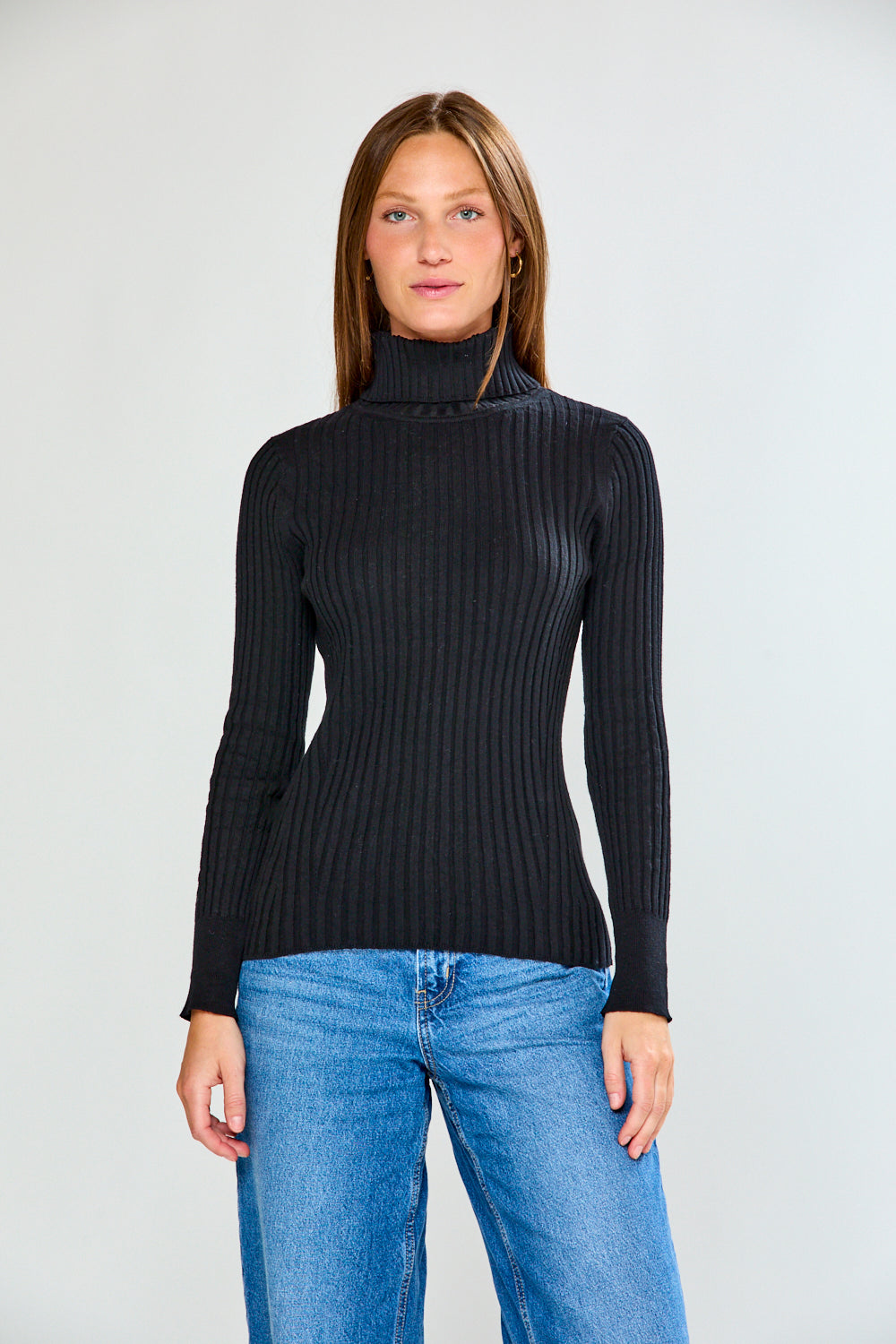 Woman wearing a black ribbed turtleneck sweater and blue jeans on a white background