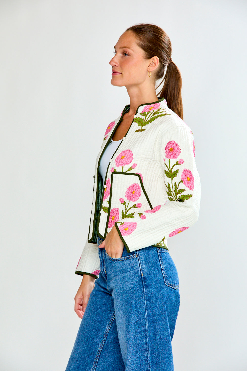 Woman wearing a floral embroidered jacket and blue jeans on a white background