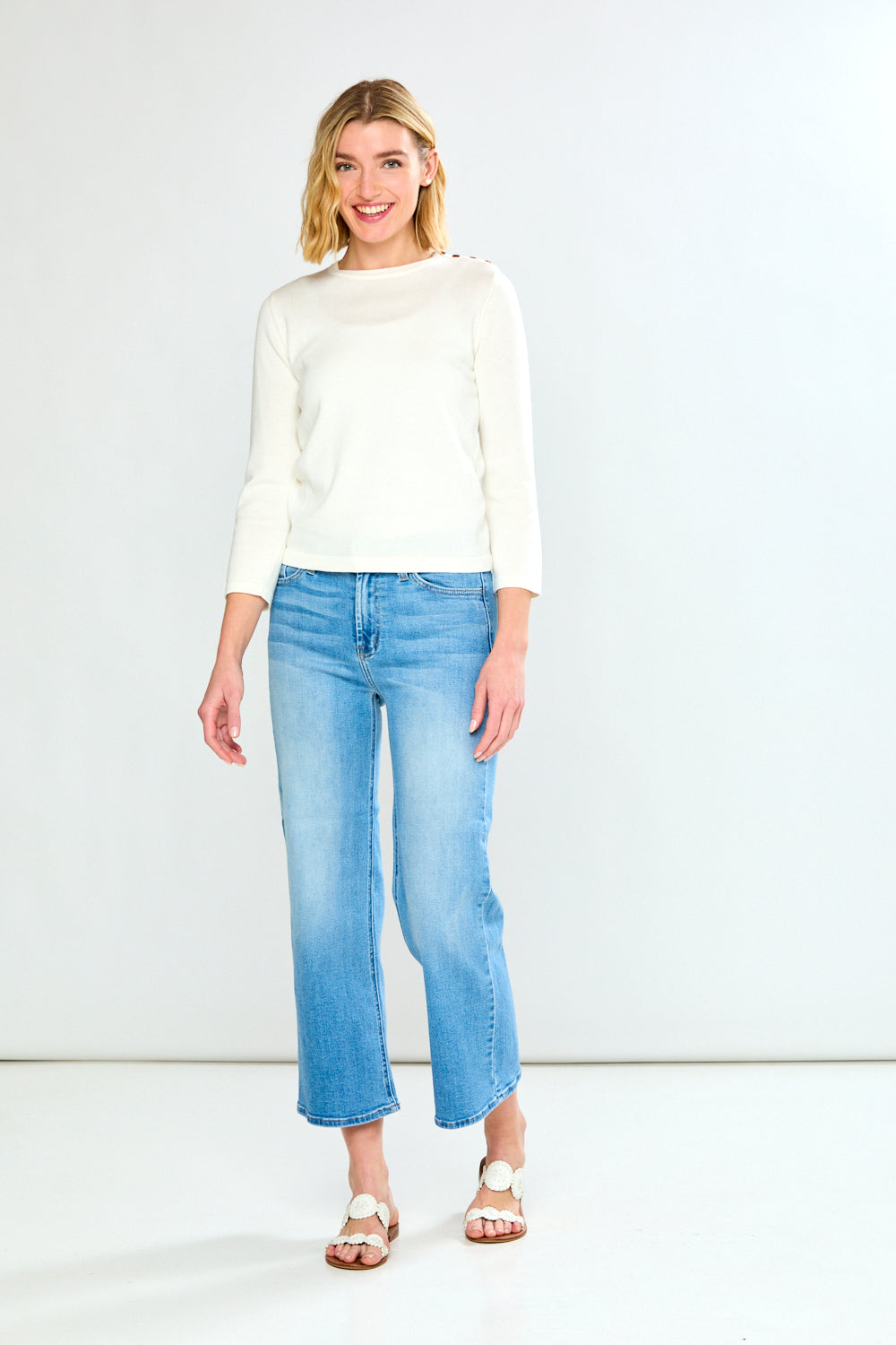 Woman wearing a white sweater and light blue jeans on a white background