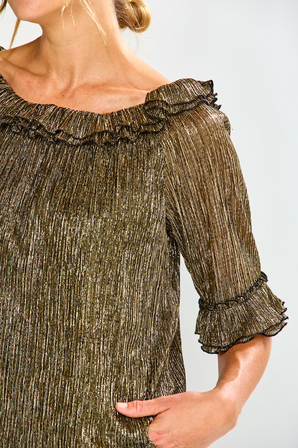 Woman wearing a gold off-shoulder top and black pants on a white background