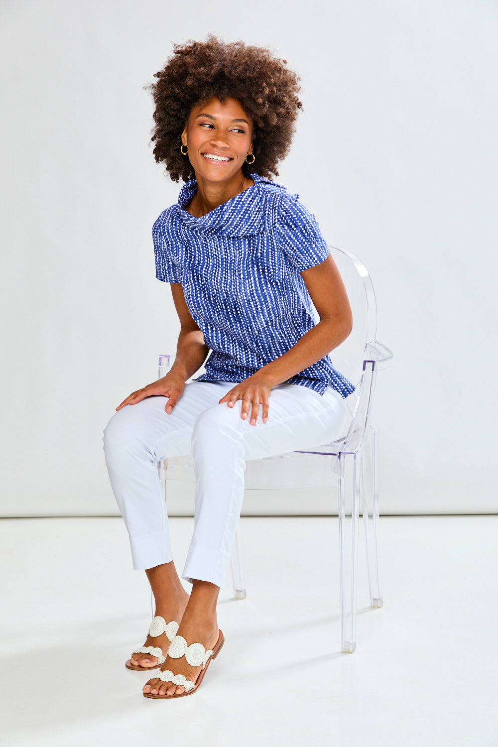 Woman wearing a blue patterned top and white pants against a plain background