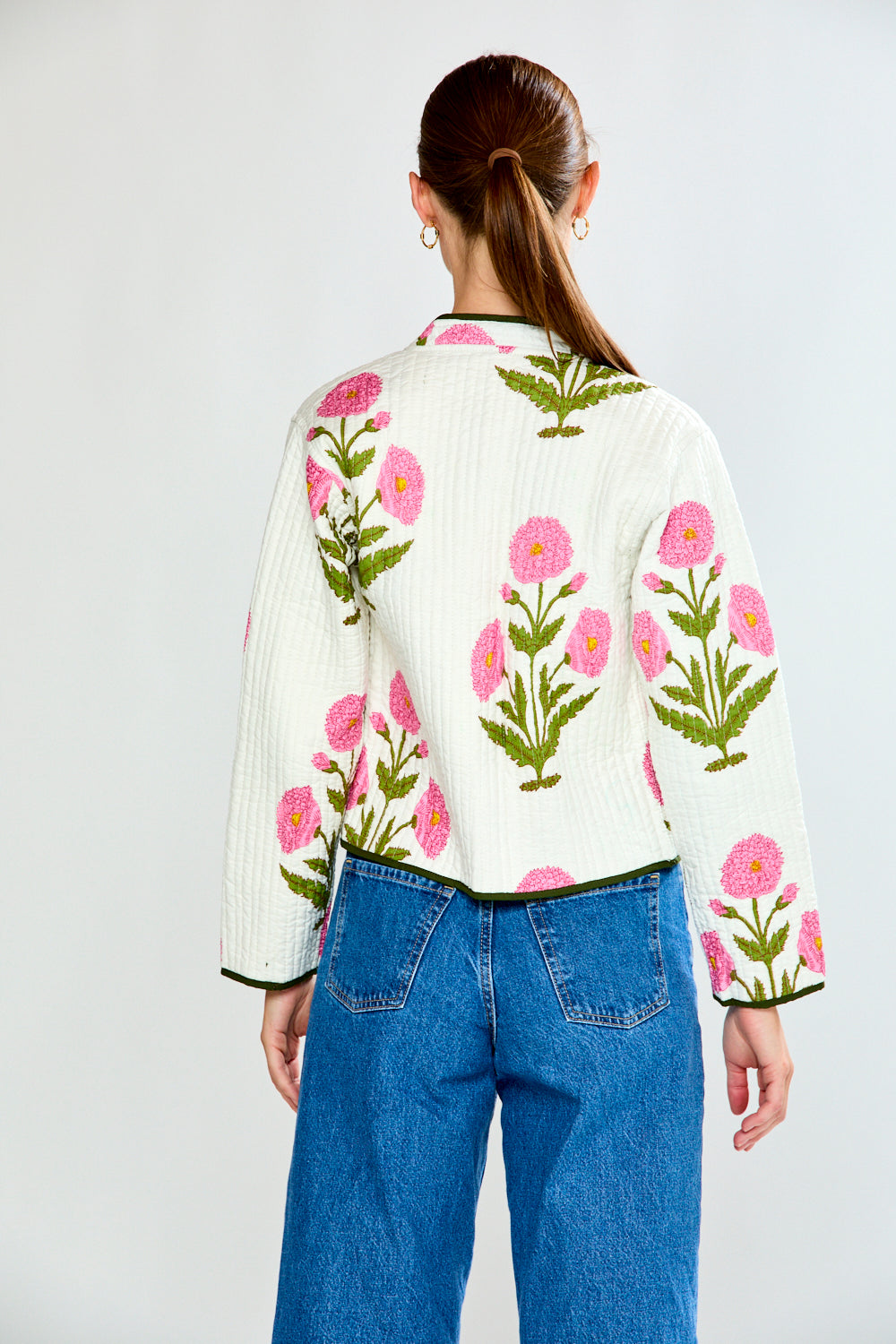 Person wearing a white blouse with pink floral patterns and blue jeans on a light gray background