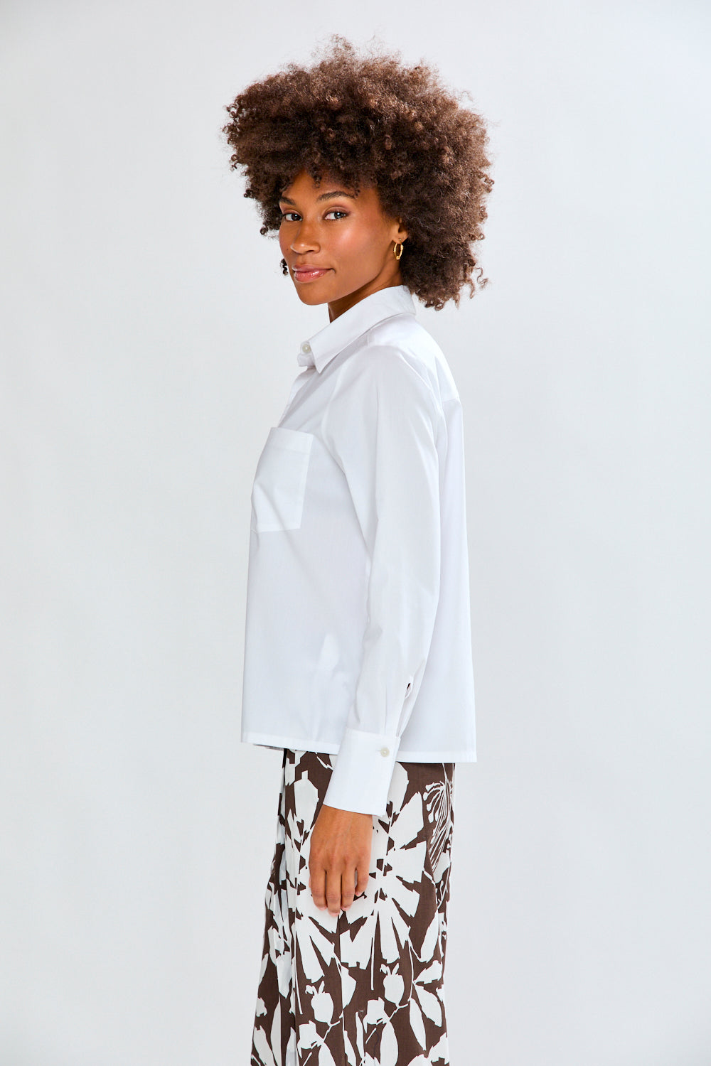 Woman wearing a white blouse and patterned pants against a plain background