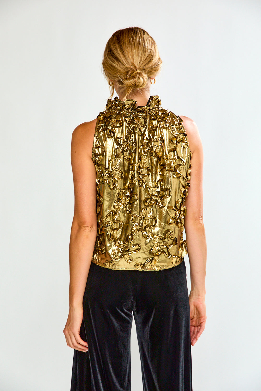 Woman wearing a gold metallic top and black pants on a white background