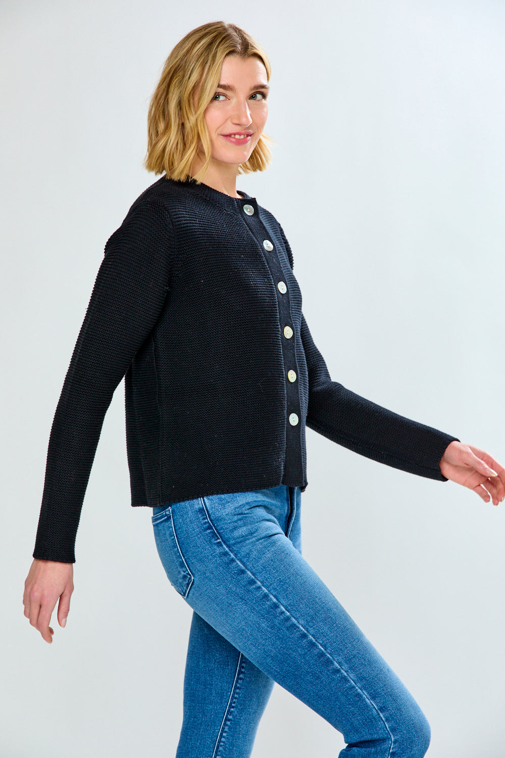 Woman wearing a black cardigan with white buttons and blue jeans on a white background