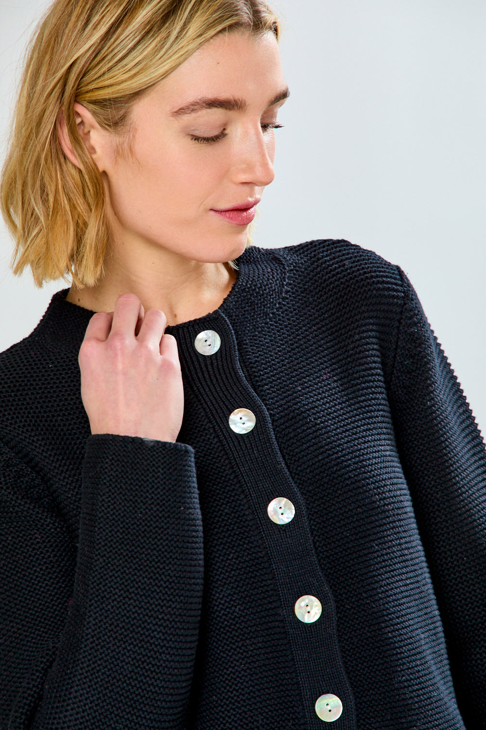 Woman wearing a dark blue knitted cardigan with white buttons on a light gray background
