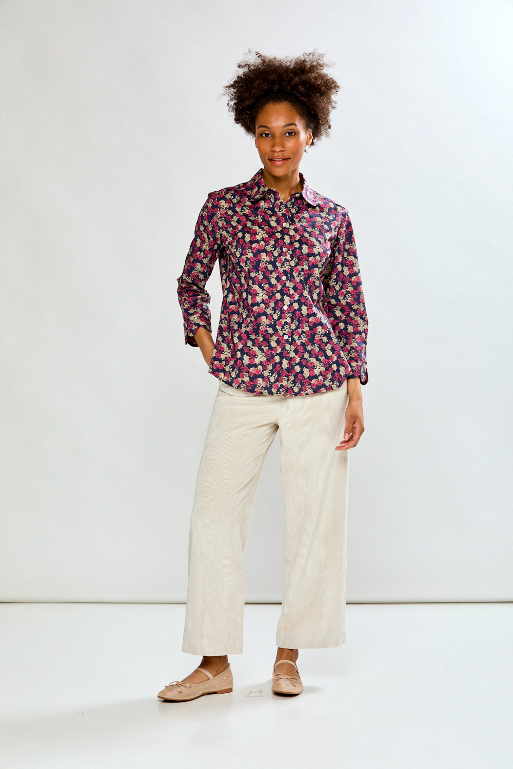 Woman wearing a patterned shirt and white pants on a white background