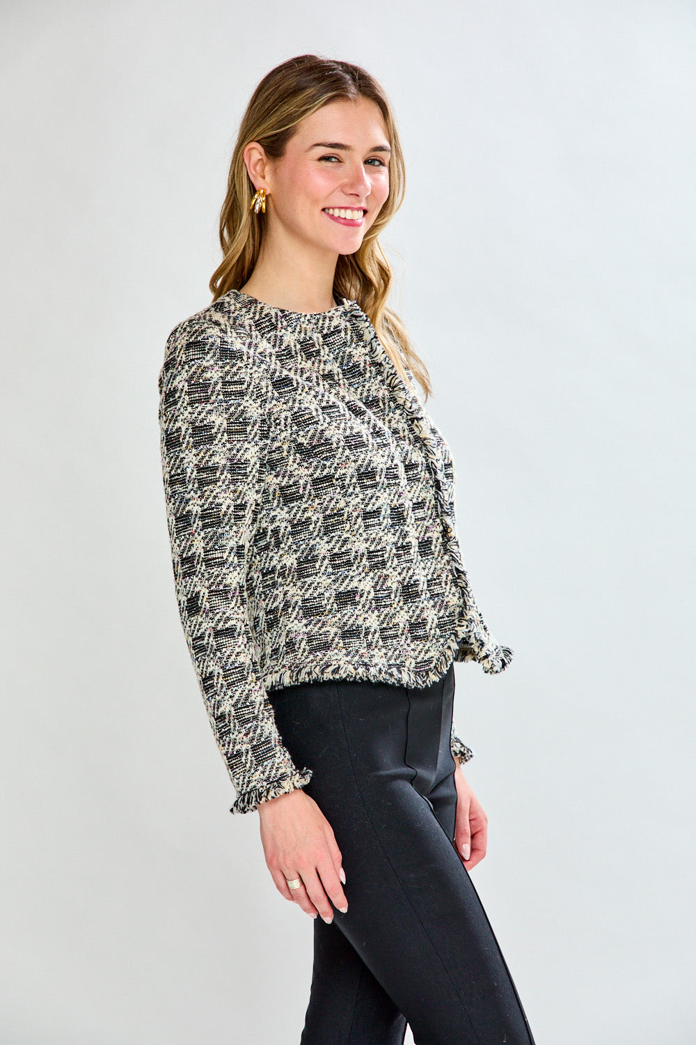 Woman wearing a black and white patterned jacket over a black top and pants on a white background
