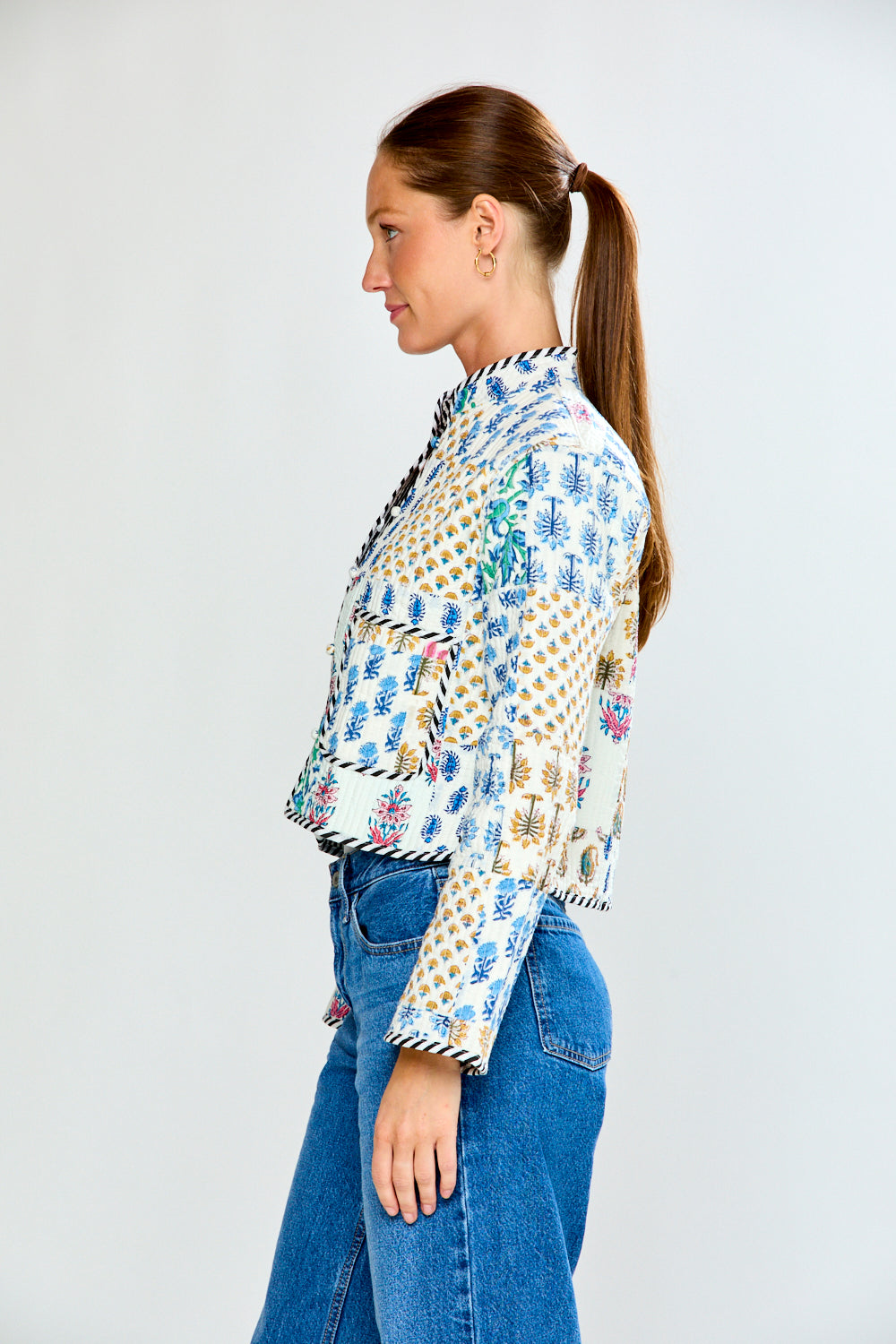 Woman wearing a patterned blouse and blue jeans on a white background