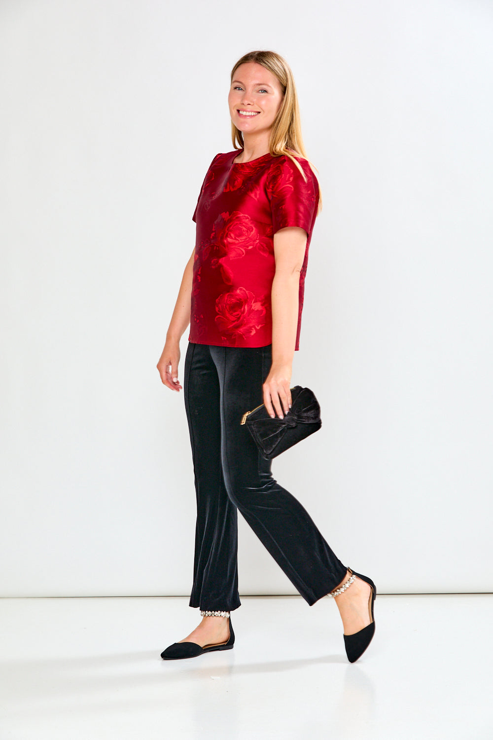 Woman wearing a red top and black pants with a white background