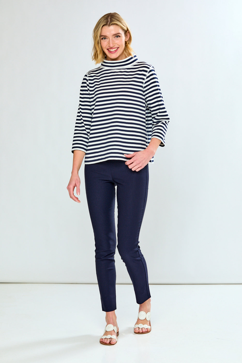 Woman wearing a striped sweater and navy pants against a white background