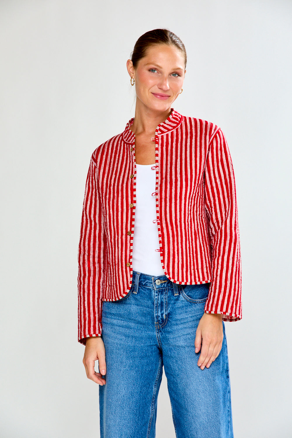 Woman wearing a red and white striped jacket with blue jeans on a plain background
