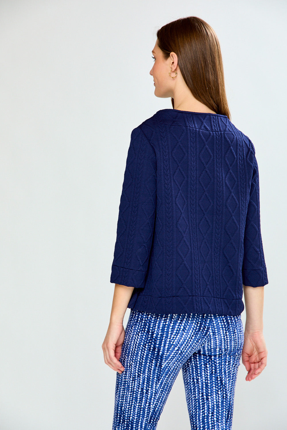 Woman wearing a navy blue cable knit top and patterned pants on a white background