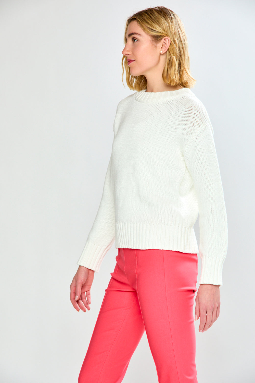 Woman wearing a white sweater and pink pants on a white background
