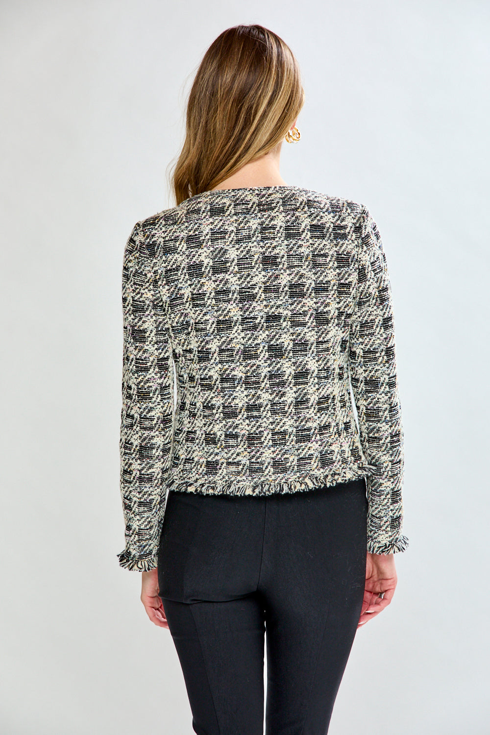 Woman wearing a black and white patterned jacket over a black top and pants on a white background