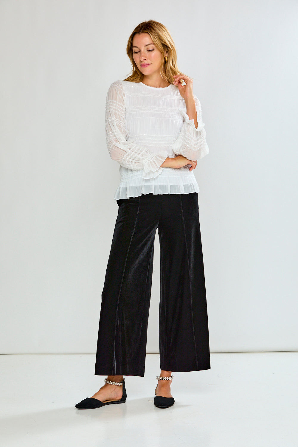 Woman wearing a white sweater and black pants against a white background