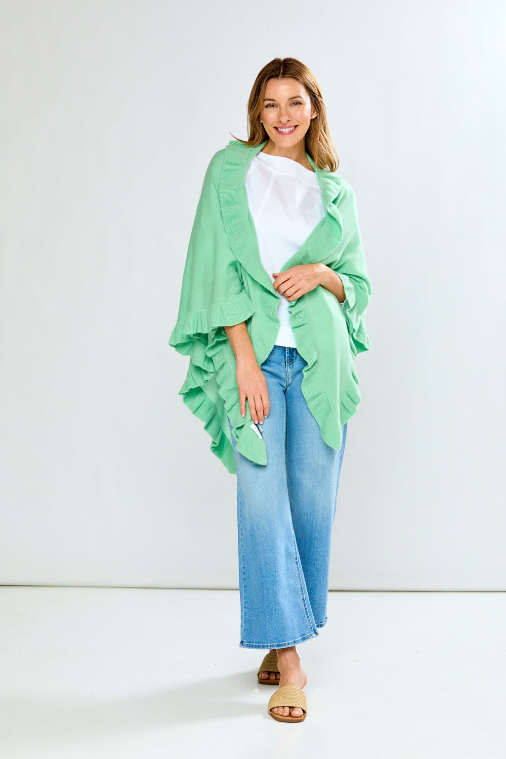 Woman wearing a light green poncho over a white shirt and blue jeans on a white background