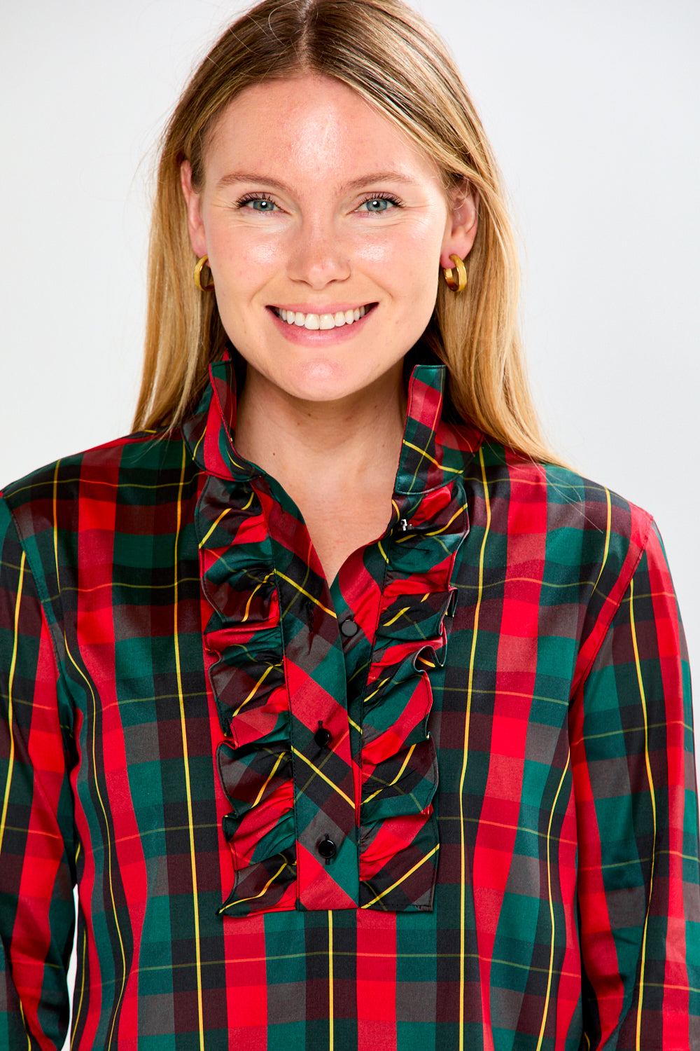 Woman wearing a red and green plaid shirt with ruffled details on a white background