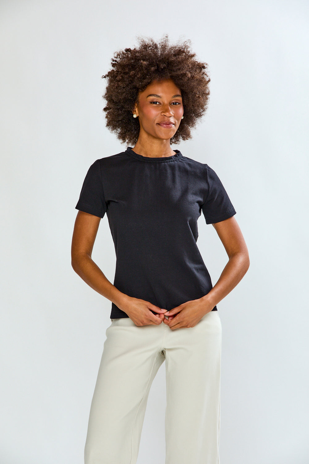 Woman wearing a black t-shirt and white pants against a plain background