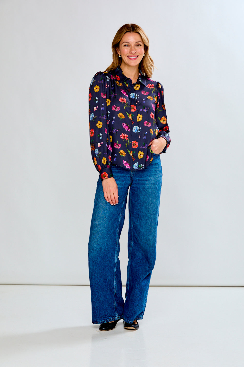 Woman wearing a colorful floral blouse and blue jeans on a white background