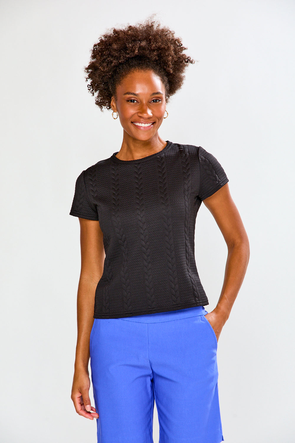 Woman wearing a black textured top and blue pants on a white background