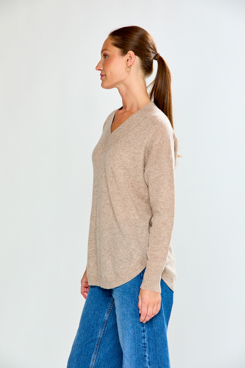 Woman wearing a beige sweater and blue jeans against a white background