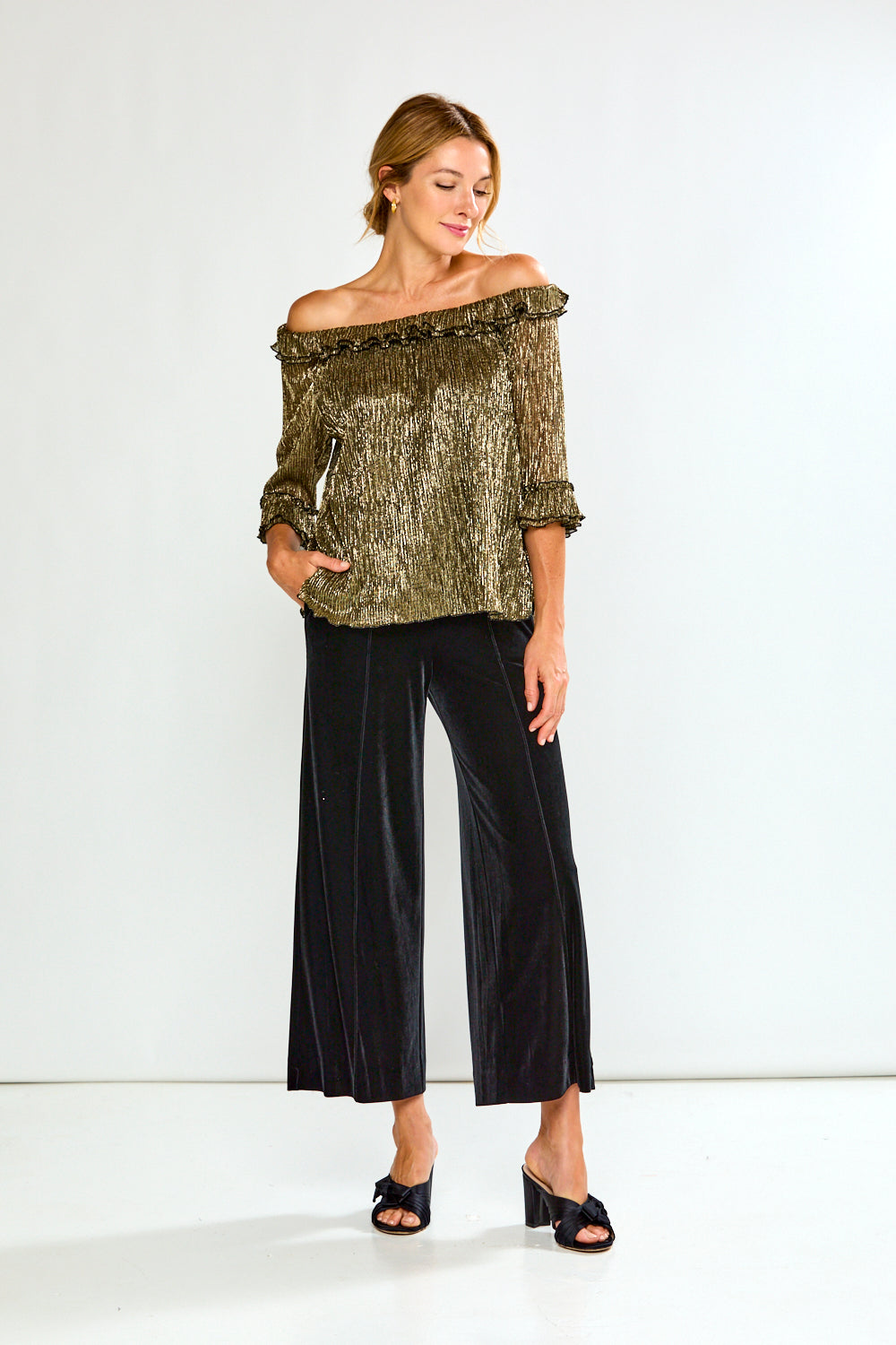 Woman wearing a gold off-shoulder top and black pants on a white background