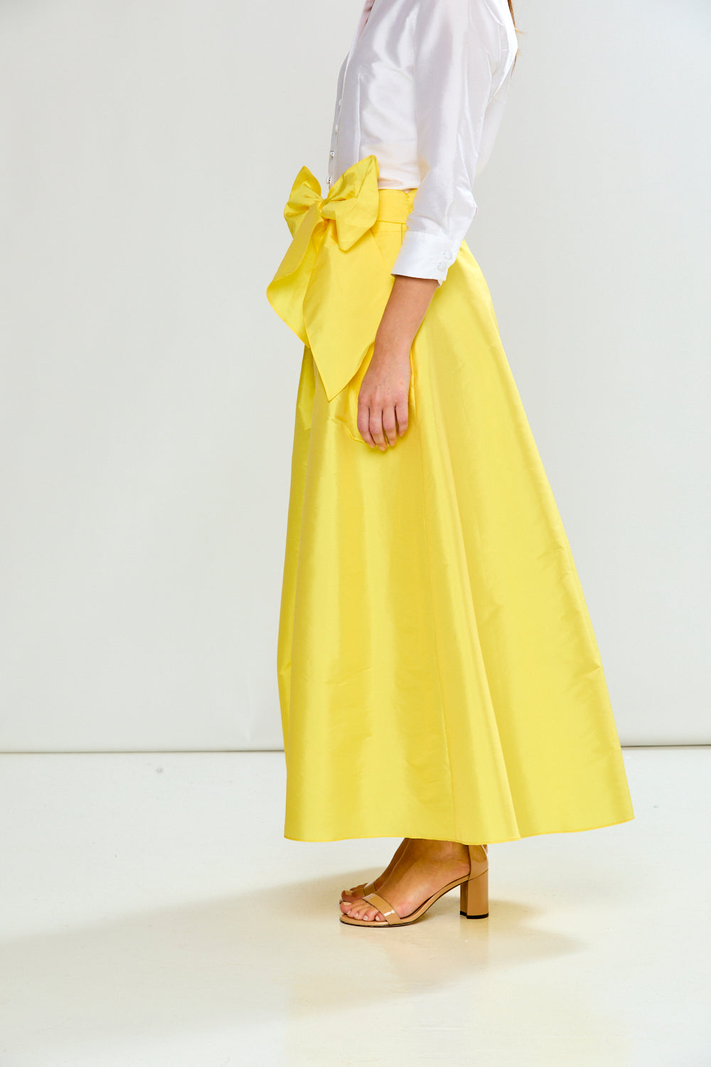 Person wearing a yellow skirt with a large bow and a white top on a white background
