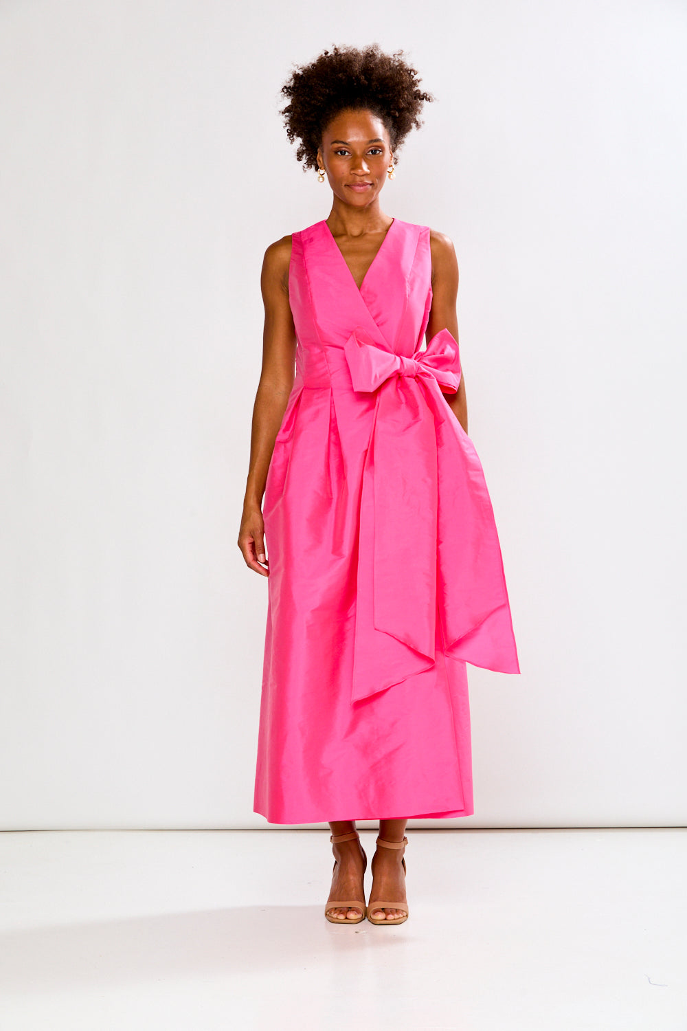 Woman wearing a bright pink dress with a bow on a white background