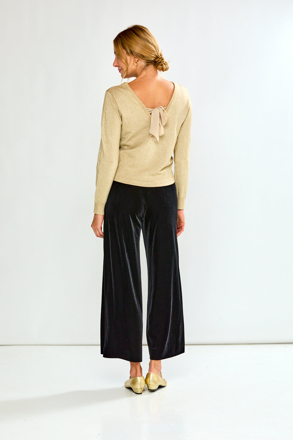 Woman wearing a gold sweater and black pants on a white background
