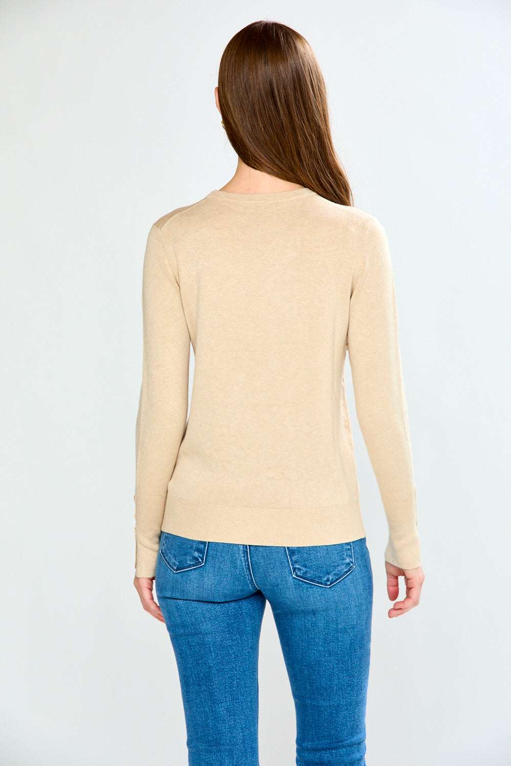 Woman wearing a sand sweater and blue jeans against a white background