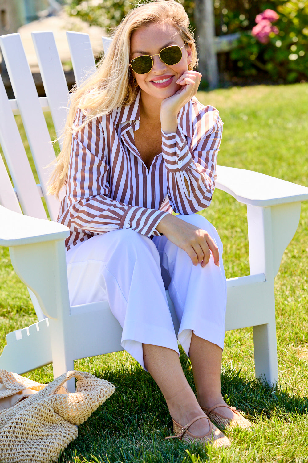 Woman sitting on a white chair outdoors, wearing a striped shirt and sunglasses.