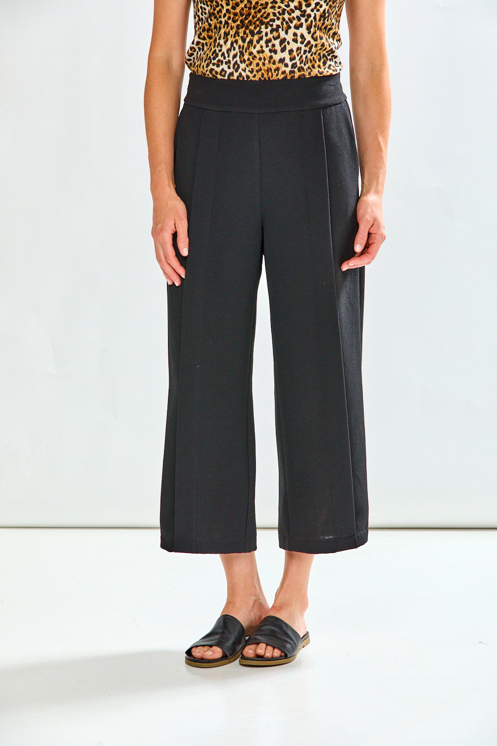 Person wearing black wide-leg pants with a leopard print top on a white background