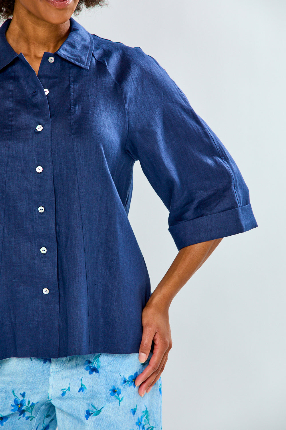 Person wearing a blue shirt with rolled-up sleeves on a plain background