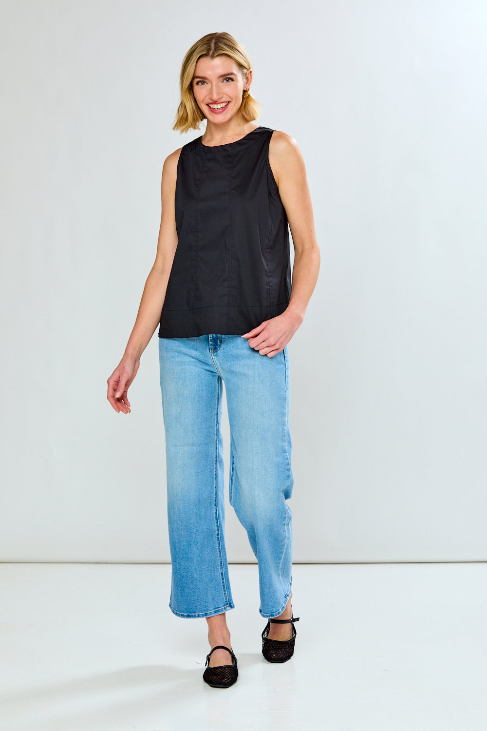 Woman wearing a black sleeveless top and light blue jeans on a white background