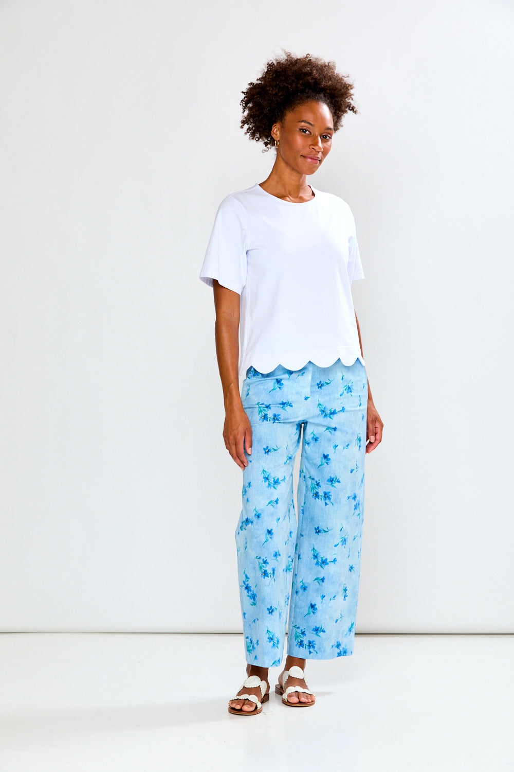 Woman wearing a white top and light blue floral pants on a white background