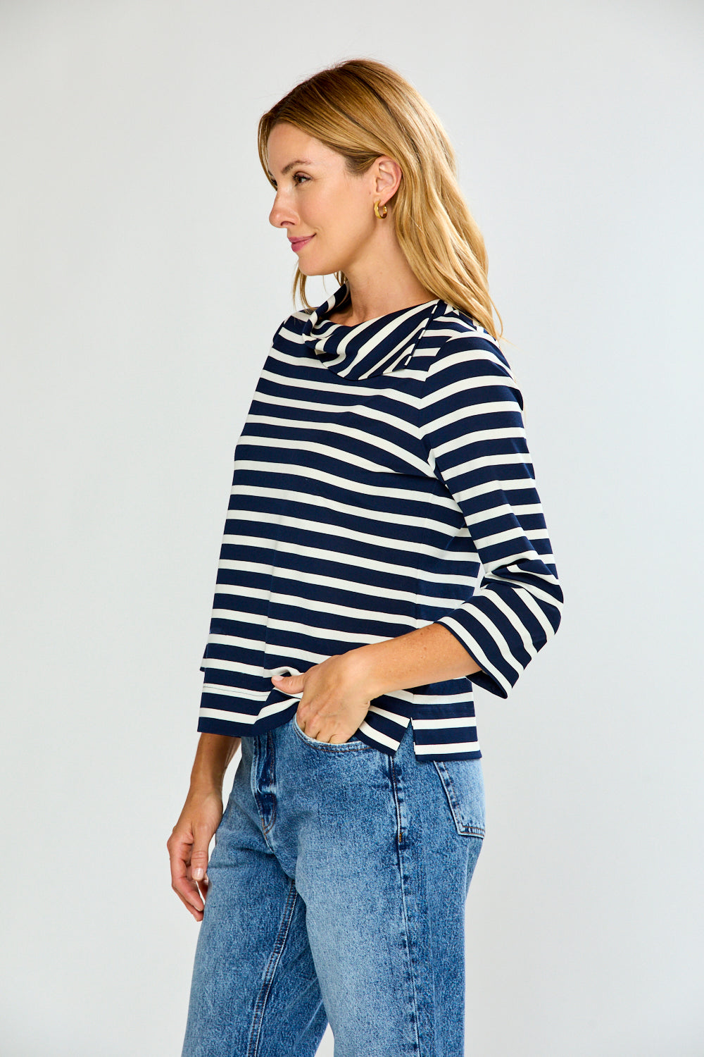 Woman wearing a navy and white striped sweater with blue jeans on a plain background