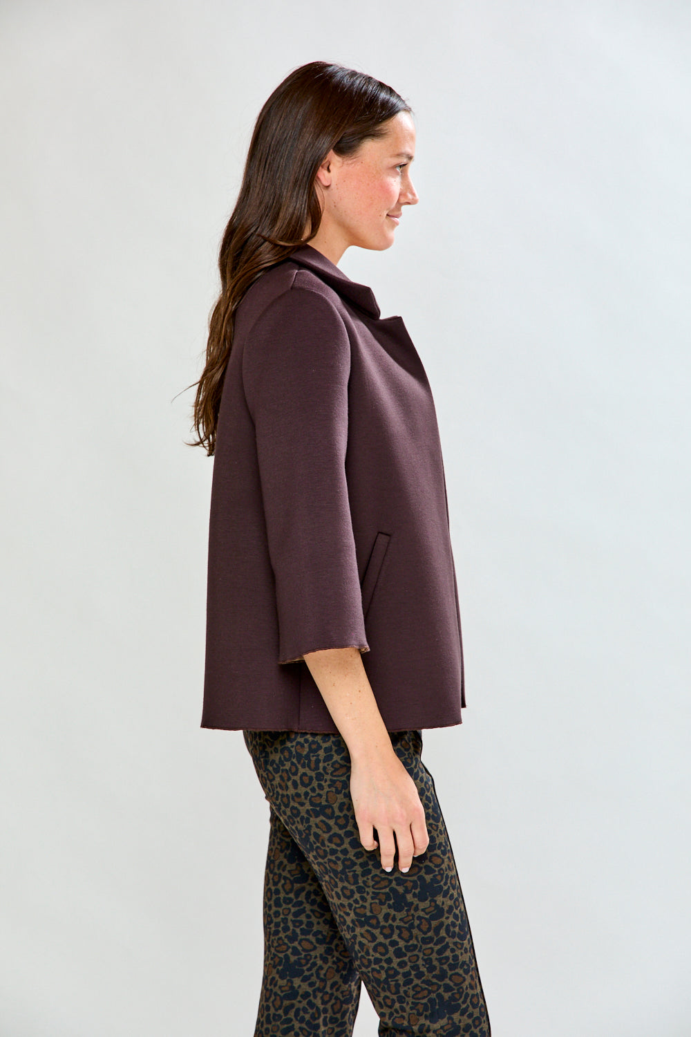 Woman wearing a brown coat and patterned pants against a white background