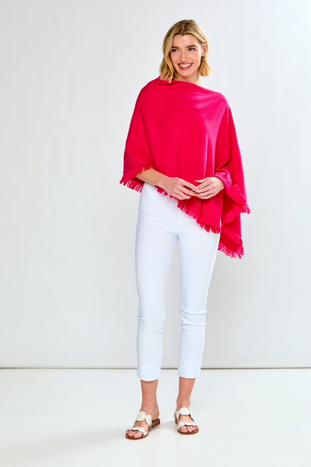 Woman wearing a bright pink poncho over a white top and pants on a white background