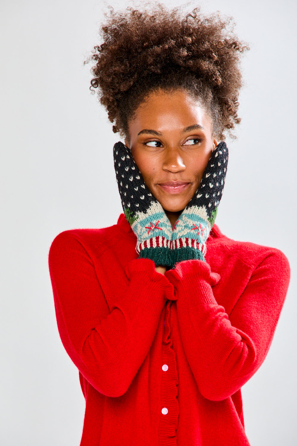 Woman wearing a red sweater and festive mittens on a plain background