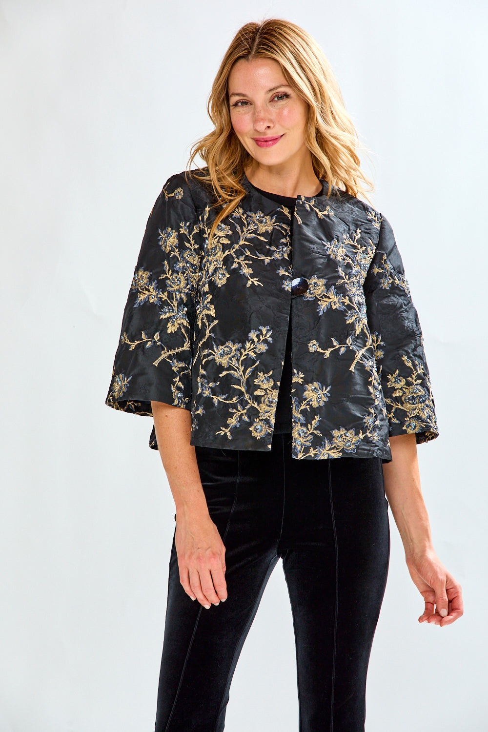 Woman wearing a black floral jacket and black pants on a white background