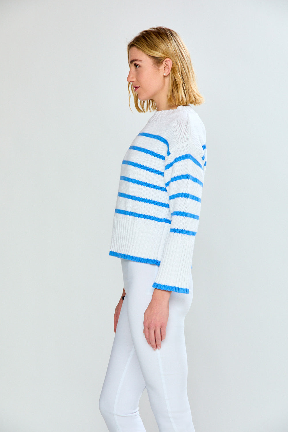 Woman wearing a white sweater with blue stripes on a plain background