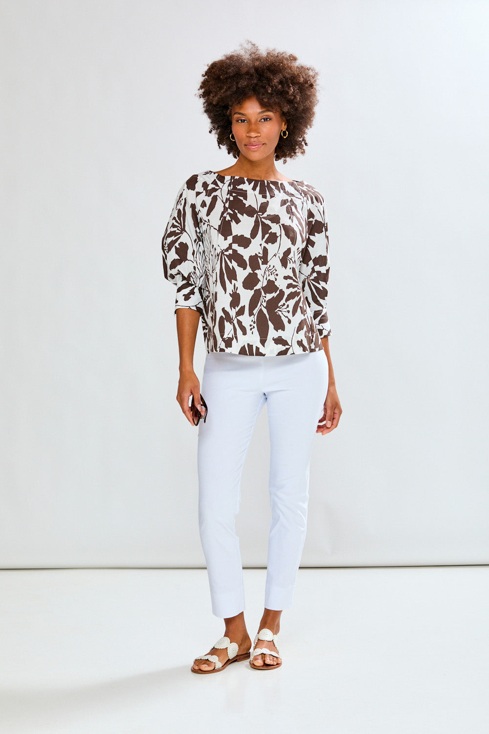 Woman wearing a patterned top and white pants against a white background