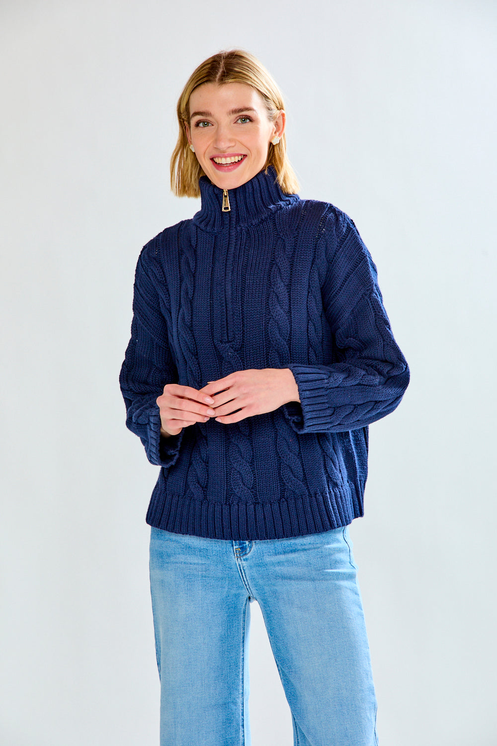 Woman wearing a navy cable knit sweater and blue jeans on a white background