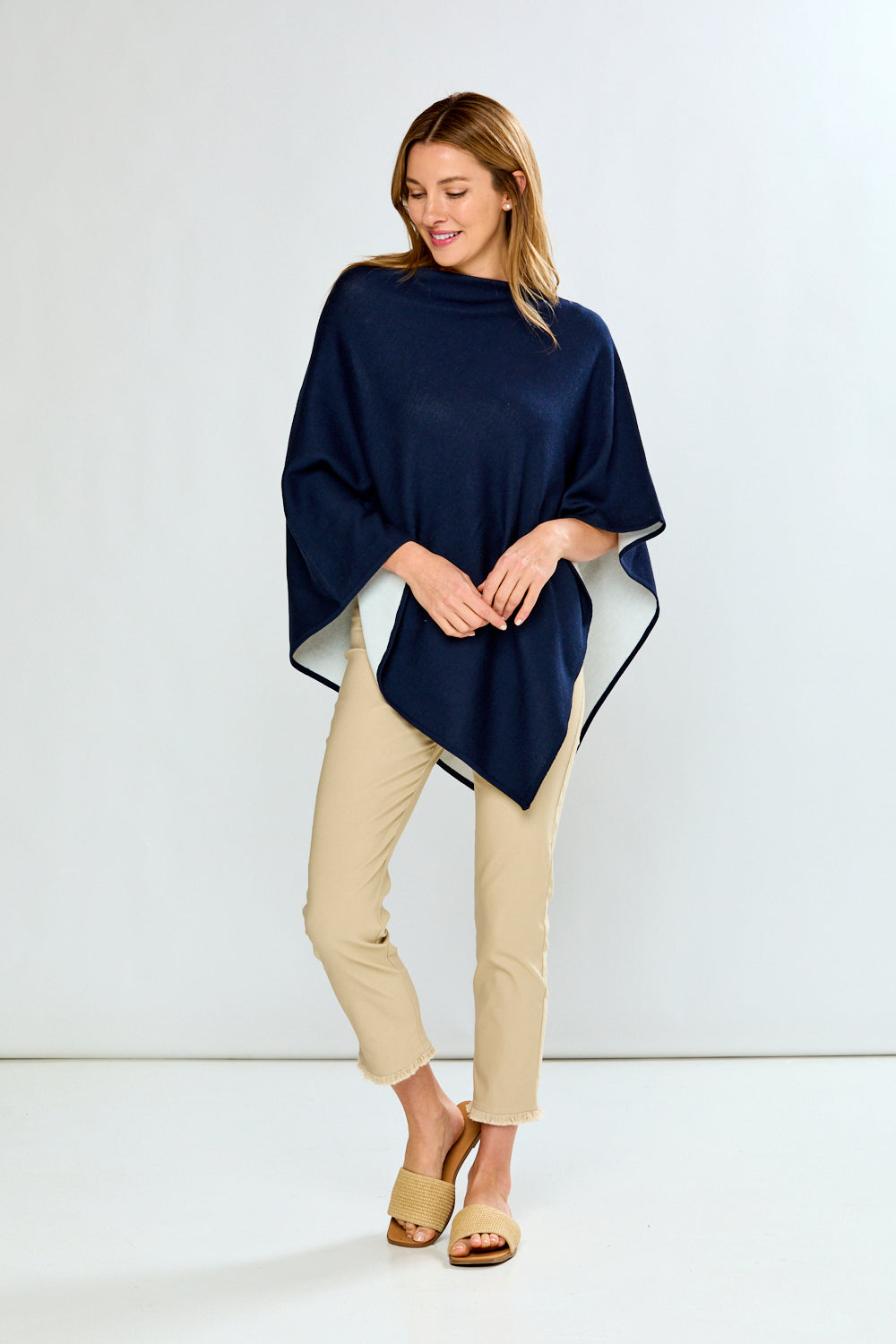 Woman wearing a navy blue poncho over a white top and beige pants on a white background